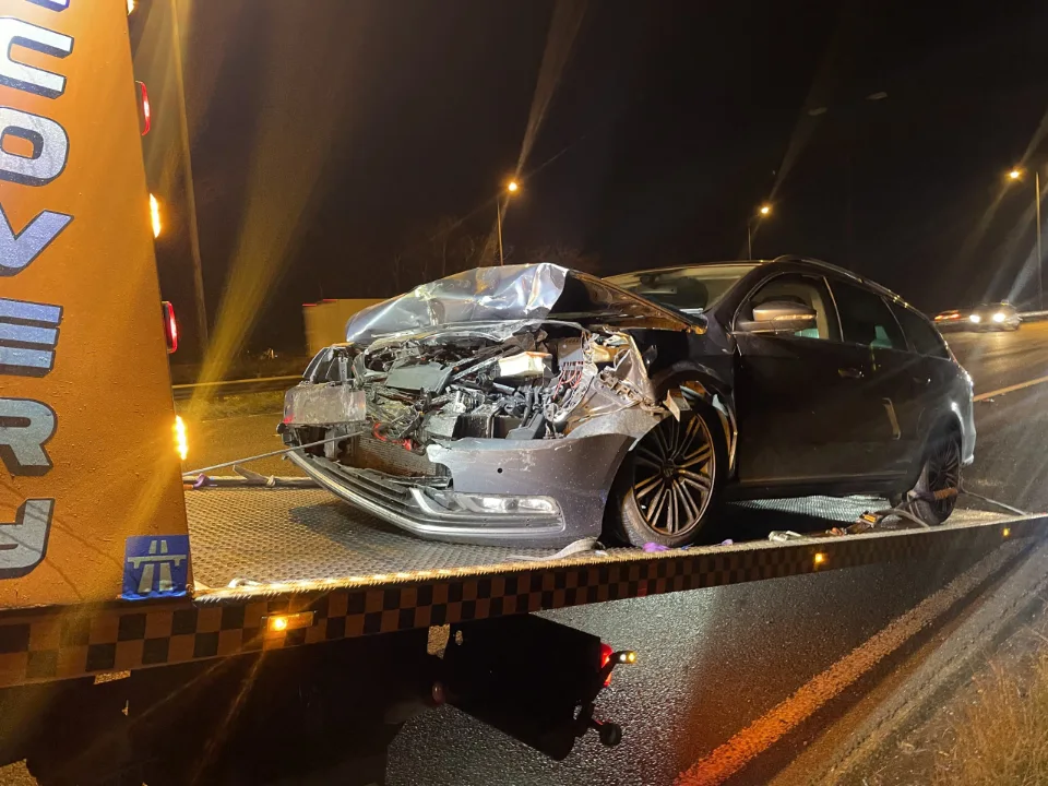 Accident-damaged car secured on a recovery truck at night
