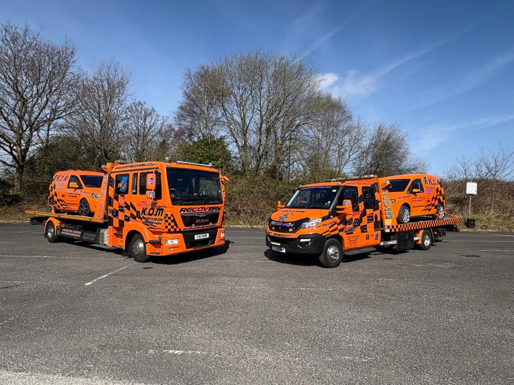 Two orange K.O.M recovery trucks carrying matching fleet vans